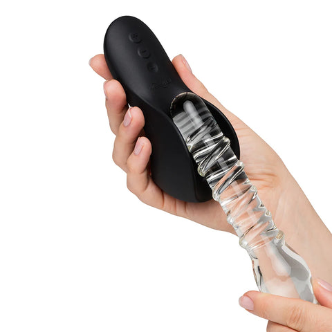 A hand holding a black personal massager with a clear glass suction-style wand attached, shown against a plain white background.